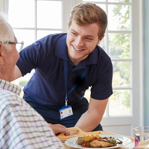 Male care worker serving dinner to elderly man